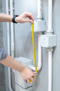 Erkek el elektrikçi elektrik boru ve duvardaki elektrik kutusu boyutunu ölçmek için mezura kullanarak. Elektrik tesisat montaj ve inşaat kavramlar bina