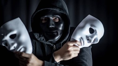 Gizem hoody giyiyor siyah maske iki beyaz maskeler elinde tutan adam. Anonim sosyal maskeleme. Major depresif bozukluk ya da bipolar bozukluk. Cadılar Bayramı kavramı