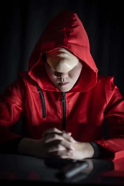 戴着红色头套的神秘男子坐在黑暗中拿着枪 犯罪和暴力概念 — 图库照片