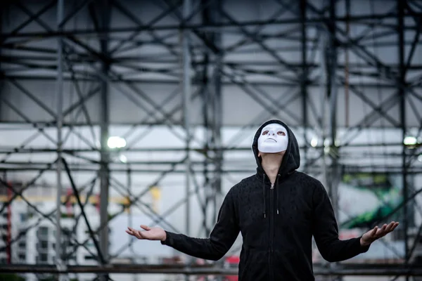Mystery hoodie man in white mask standing in the rain looking up at the sky on rooftop of abandoned building. Bipolar disorder or Major depressive disorder. Depression concept