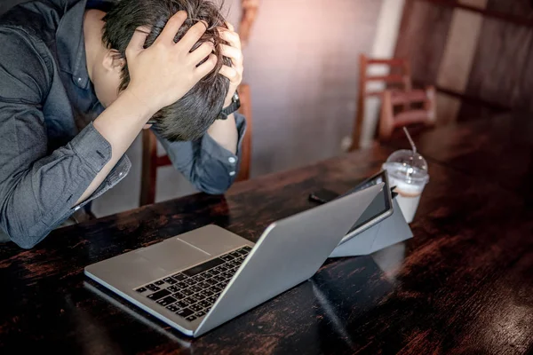 Overworked Asian businessman or male entrepreneur feeling stressed and frustrated while working with laptop computer and digital tablet in the cafe. Tired and headache from work hard or failure.