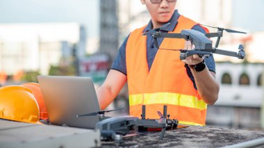 Dron, uzaktan kumanda ve dizüstü bilgisayar ile inşaat alanında çalışan Asya mühendis adam. İnsansız hava aracı (İHA) arazi için kullanarak ve inşaat mühendisliği proje sitesi anket oluşturma.
