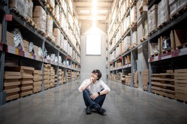 Karton rafların arasında oturan Asyalı alışverişçi depoda ne alacağına karar veriyor. Mağazada alışveriş yaşam tarzı. Fabrika malları almak ya da satın almak. Envanter endüstrisi konsepti