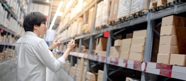 Asya'ya ait adam alışveriş Smartphone cep telefonu ile alışveriş listesi denetimi ambar Stok koridoru ayakta. Satın alma veya fabrika mal satın alma. Alışverişkoliğin kavramı