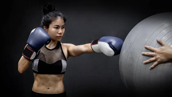 Young Asian girl boxer in sportswear punching exercise ball with blue boxing gloves in fitness gym. Martial arts training concept