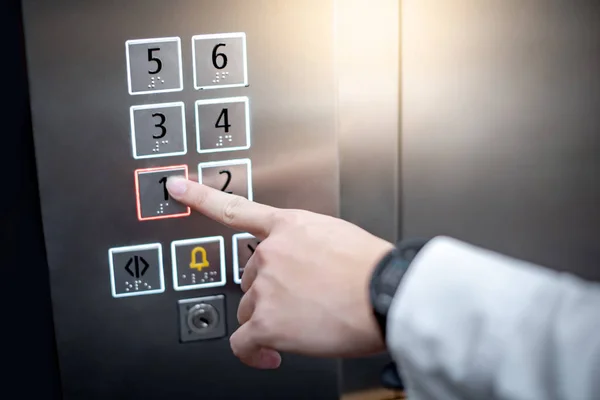 Male forefinger (index finger) pressing on the first floor button or floor number one in elevator (lift). Mechanical engineering concept