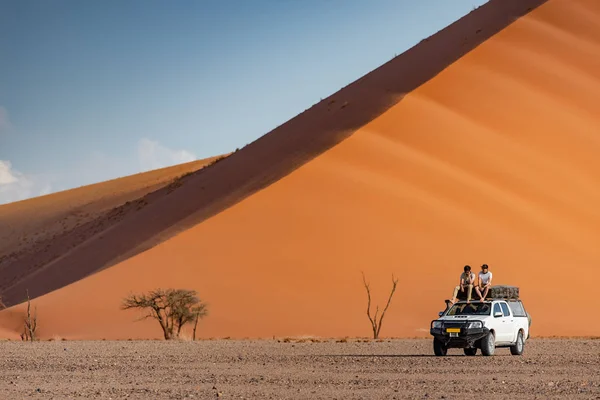 两个亚洲男人旅行者和摄影师坐在橙色沙丘附近的野营车 旅行沙漠概念 — 图库照片