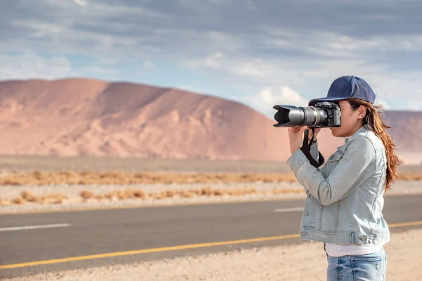 若いアジア女性旅行者と砂丘のカメラ撮影写真を保持している写真家 アフリカのナミビアのナミブ砂漠では 道路の近きます 旅行写真コンセプト — ストック写真