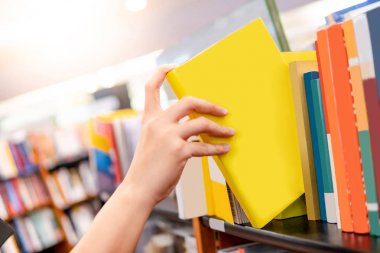 Kitaplıktan sarı kitap seçen erkek el