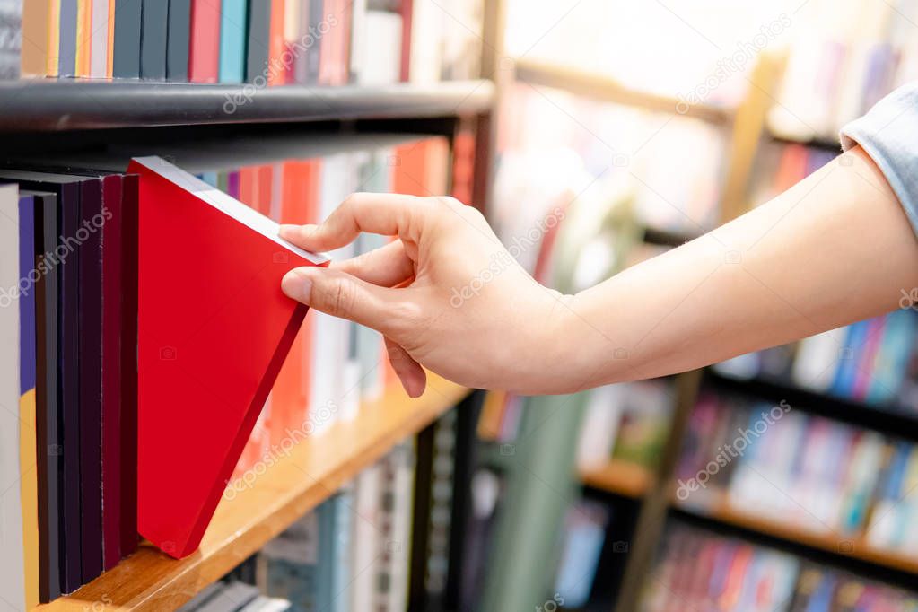 Male hand choosing red book from bookshelf