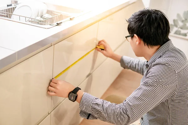 Asian man using tape measure on kitchen counter