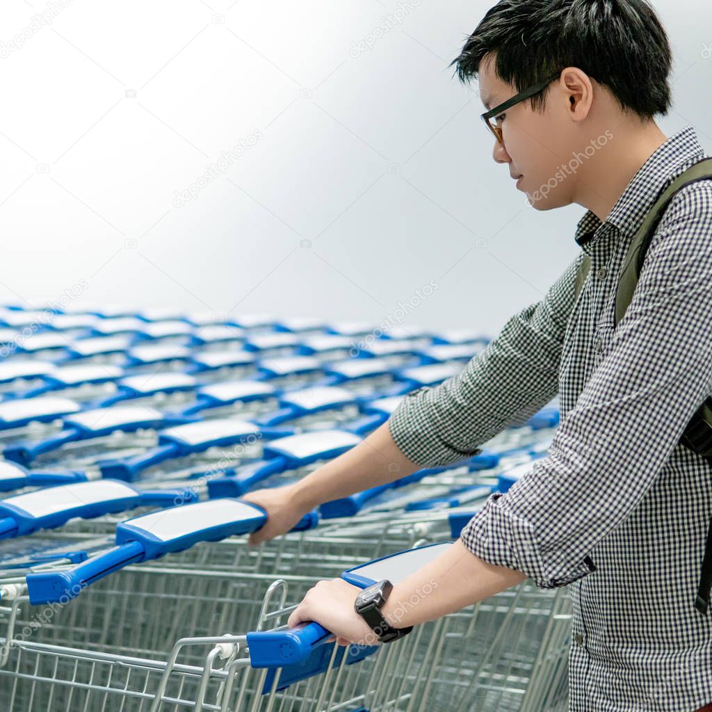 Asian man pulling shopping cart in supermarket