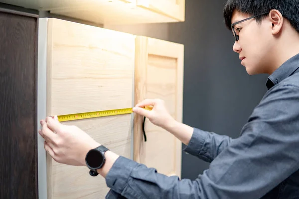 Asian man using tape measure on cabinet materials