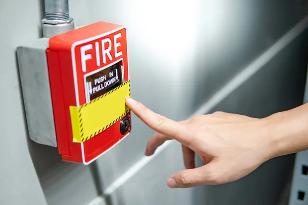 Hand pointing at fire alarm switch on the wall