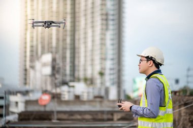 Asyalı mühendis, şantiyeüzerinde insansız hava aracı uçuruyor. İnşaat mühendisliği projesinde arazi ve şantiye araştırması için insansız hava aracı (İhA) kullanan erkek işçi.