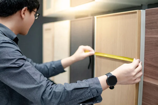 Asian man using tape measure on cabinet materials