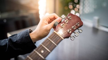 Erkek el, akustik gitarın vidalarını ayarlıyor.