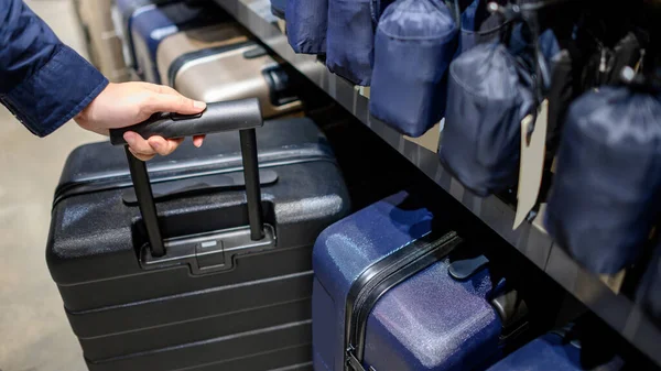 Male hand customer choosing black suitcase luggage at shop in department store. Shopping small size travel baggage for business trip.