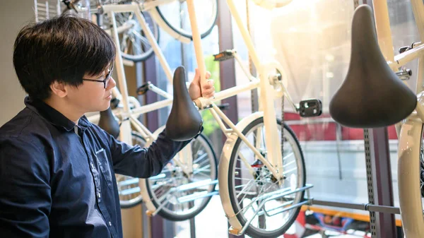 Asian man in casual clothing choosing new bicycle in bike shop. Shopping bicycle for urban sporty lifestyle.
