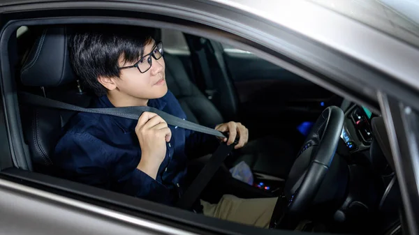 Driving safety concept. Asian businessman fasten seat belt while sitting on driver seat in modern car. Land vehicle for urban lifestyle.