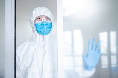 Hastane kliniğinin kapısında duran doktor ya da doktor kişisel koruyucu ekipman. Koronavirüsü (COVID-19) enfeksiyonunu önlemek için PPE giysisi, maskesi ve gözlüğü olan bir tıp çalışanı.