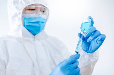 COVID-19 Aşı Konsepti. Coronavirus aşısı enjeksiyonu için şırınga ve ilaç şişesi tutan maske, gözlük ve lastik eldivenli kişisel koruyucu ekipman giysisi (PPE) giyen doktor veya hekim.