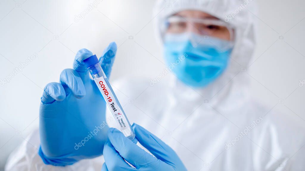Medical scientist man in personal protective equipment suit (PPE), mask and gloves holding COVID-19 Test tube in hospital laboratory. Male doctor getting result of Coronavirus case. 2019-nCoV research