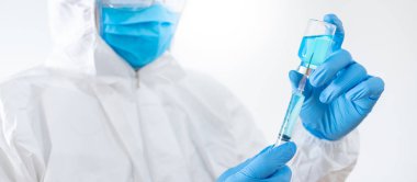 COVID-19 Aşı Konsepti. Coronavirus aşısı enjeksiyonu için şırınga ve ilaç şişesi tutan maske, gözlük ve lastik eldivenli kişisel koruyucu ekipman giysisi (PPE) giyen doktor veya hekim.