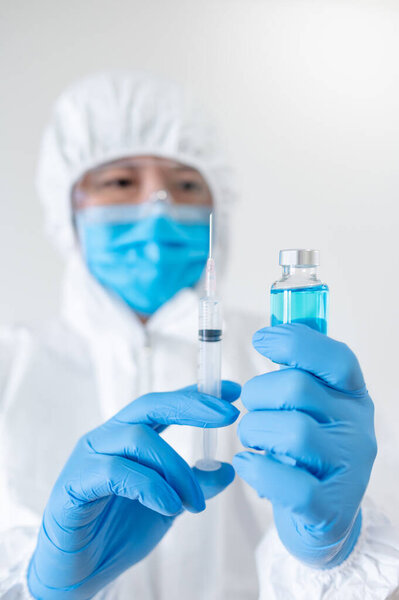 Концепция вакцинации COVID-19. Врач или врач в защитном костюме (СИЗ) с маской, очками и резиновыми перчатками, держащими шприц и медицинский флакон для инъекции коронавируса
.