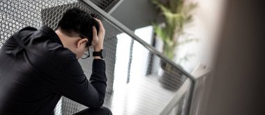 Asyalı işadamı stresli hissediyor ve ofis binasındaki merdivenlerde otururken baş ağrısı çekiyor. İş probleminin bunalımı. Ruh sağlığı hastalığı ya da ofis sendromu kavramı