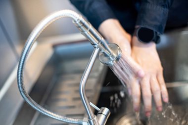 Modern paslanmaz muslukla mutfak lavabosunda el yıkamak. Su kavramı kaydediliyor