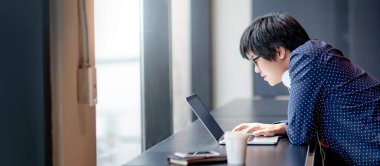 Ofiste dizüstü bilgisayarla çalışan gözlüklü ve kulaklıklı Asyalı bir iş adamı. Modern teknolojiyle akıllı çalışın..