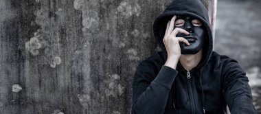 Kapüşonlu ceketli, siyah maskeli gizemli adam terk edilmiş binada oturmuş yorgun ve stresli hissediyor. Depresyon (büyük depresif bozukluk) veya zihinsel sağlık sorunları kavramları.