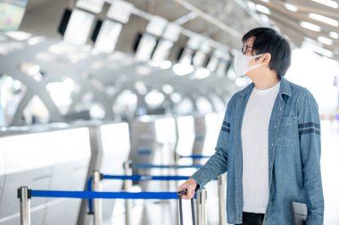 Havaalanı terminalinde bavul taşıyan yüz maskesi takan Asyalı bir turist. Coronavirus (COVID-19) seyahat ederken salgını önler. Sağlık farkındalığı ve sosyal uzaklık