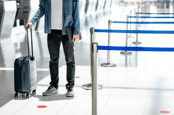 Travel insurance concept. Male tourist carrying suitcase luggage and digital tablet waiting for check in and baggage claim at airline counter in airport terminal.