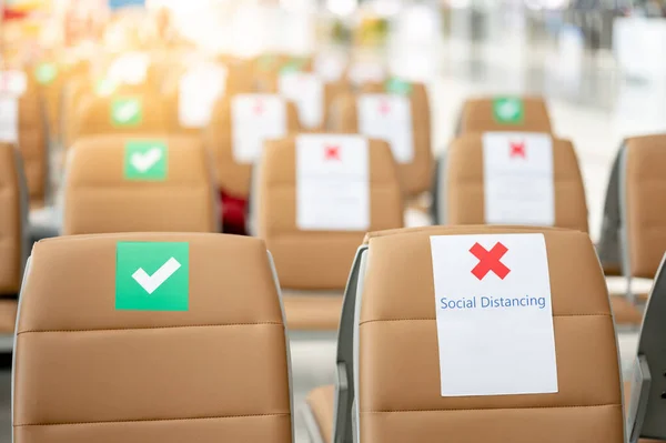 Social distancing or physical distancing concept. Correct and cross symbol on seat at waiting area of airport terminal. Guidance sticker show to keep distance while sitting public building.