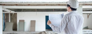 Asyalı inşaat mühendisi ya da koruma kaskı takan inşaat işçisi. Elinde planlar var. İnşaat alanında çalışan erkek mimar. İnşaat ve mimari tasarım kavramları