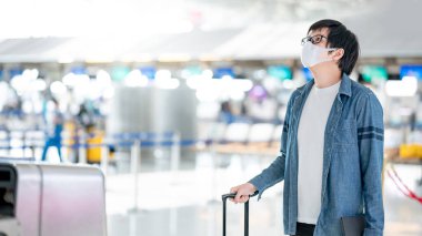 Havaalanı terminalinde bavul taşıyan yüz maskesi takan Asyalı bir turist. Coronavirus (COVID-19) seyahat ederken salgını önler. Sağlık farkındalığı ve sosyal uzaklık