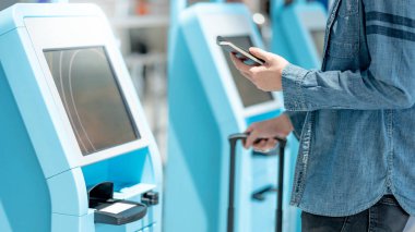 Pasaportu ve akıllı telefonu olan bir erkek turist havaalanı terminalinde kendini kontrol gişesini kullanıyor. Yurt dışına seyahat kavramı
