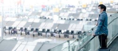 Havaalanı terminalinin kapısında maskeli Asyalı bir turist bekliyor. Coronavirus (COVID-19) seyahat ederken salgını önler. Sağlık farkındalığı ve sosyal uzaklık