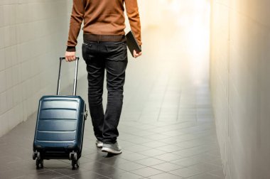 Seyahat sigortası konsepti. Havaalanı terminalinde valiz ve dijital tablet taşıyan bir erkek turist yürüyor.