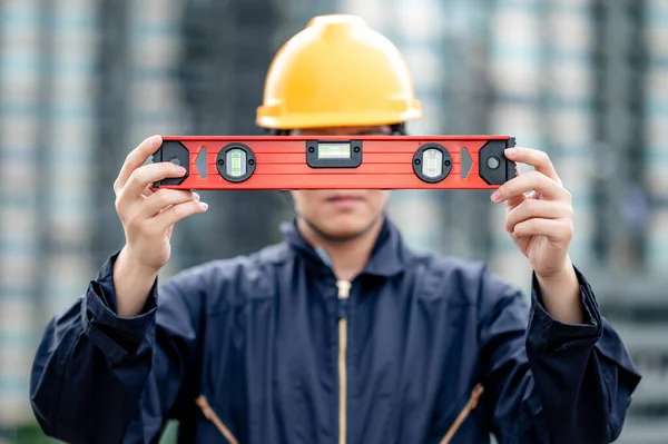 Asian maintenance worker man holding red aluminium spirit level tool or bubble levels at construction site. Equipment for civil engineering project