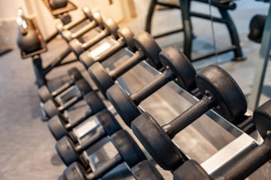Spor salonunda askıda duran bir grup siyah metal halter. Spor fitness merkezinde ağırlık eğitimi ekipmanları. Kas geliştirme konsepti