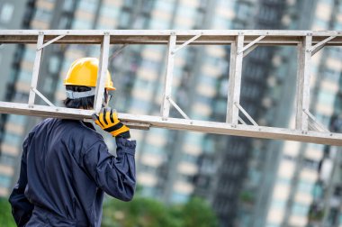 İnşaat alanında alüminyum merdiven taşıyan koruyucu giysili ve kasklı Asyalı tamirci. İnşaat mühendisliği, mimarlık, inşaat ve inşaat hizmeti kavramları.