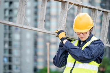 İnşaat alanında alüminyum merdiven taşıyan güvenlik kasklı ve yansıtıcı kıyafetli Asyalı tamirci. İnşaat mühendisliği, mimarlık, inşaat ve inşaat hizmeti kavramları.