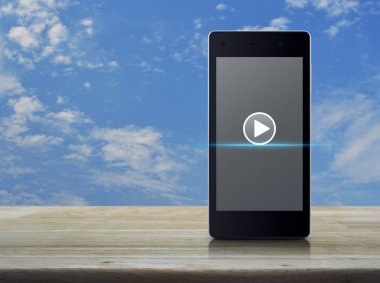 Ahşap masa mavi gökyüzü ile beyaz bulutlar, iş müzik online kavramı üzerinde modern akıllı telefonun ekranında Oynat düğmesini