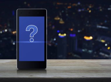 Ahşap masa bulanıklık renkli gece ışık şehir Kulesi, müşteri destek kavramı üzerinde modern akıllı telefonun ekranında üzerinde soru işaretinin görüntülenmesi
