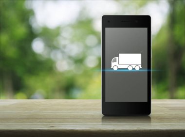 Kamyon düz ahşap masa üzerinde modern akıllı telefonun ekranında simgesine bulanıklık yeşil ağaç Park, iş ulaşım hizmeti kavramı