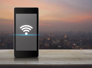 Ahşap masa cityscape bulanıklık sıcak ışık gün batımından üzerinde üzerinde modern akıllı telefonun ekranında Kablosuz bağlantı simgesine kavramı, teknoloji ve internet
