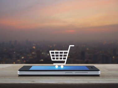 Alışveriş sepeti simgesine ahşap masa üzerinde modern akıllı telefonun ekranında bulanıklık cityscape sıcak ışık sundown, alışveriş online kavramı